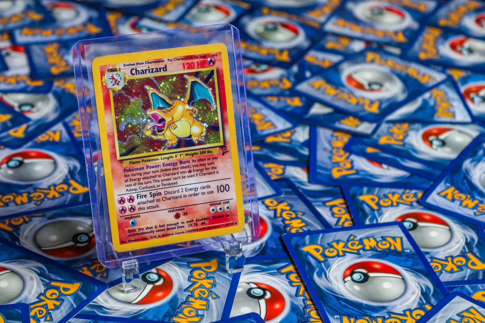 A Charizard card in a protective case standing on a spread of Pokémon cards