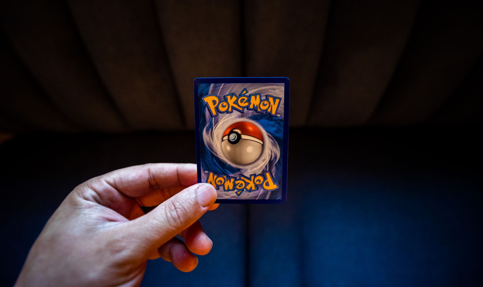 A hand holding up a Pokémon card against a dark background